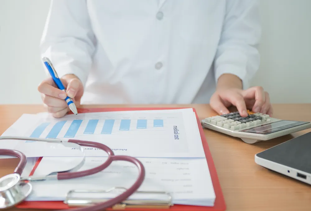 Doctor calculating medical costs next to a chart and stethoscope