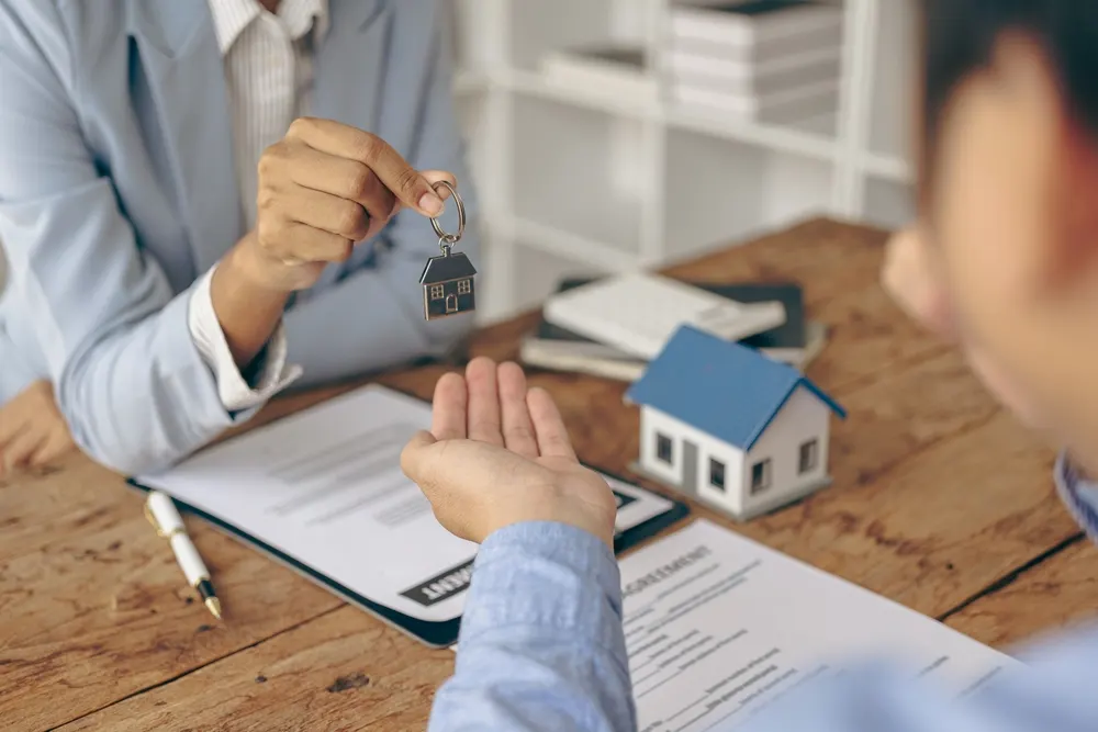 House key and model home on a desk with property and asset protection documents