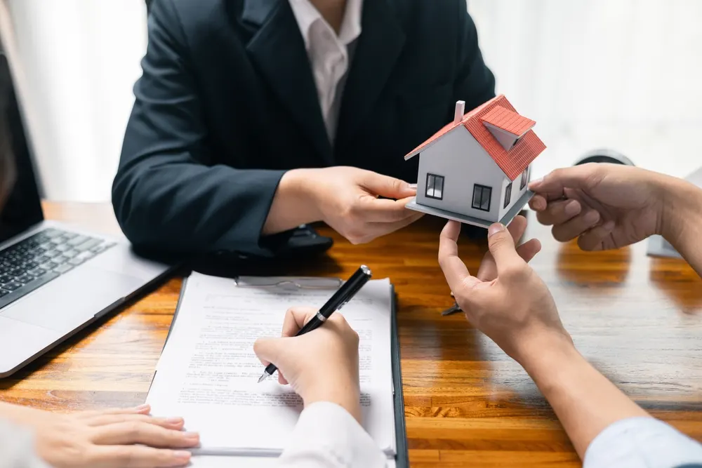 An advisor handing over a model house to a client signing a document
