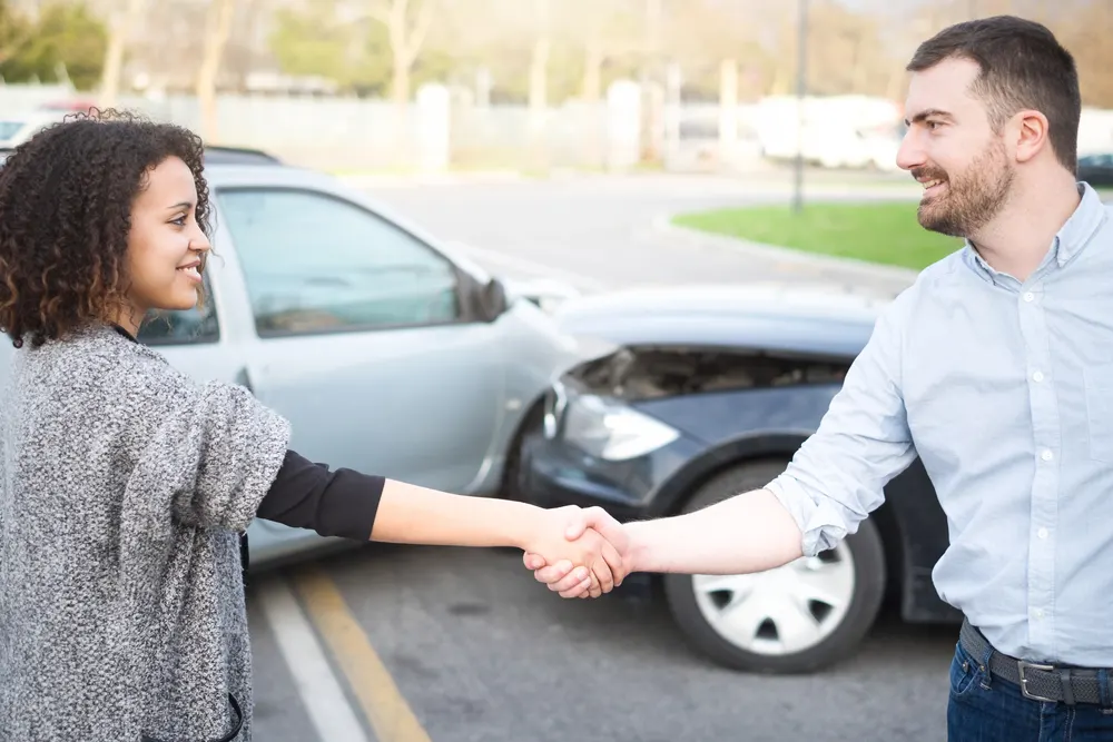 Two people shaking hands near damaged vehicles after a car accident