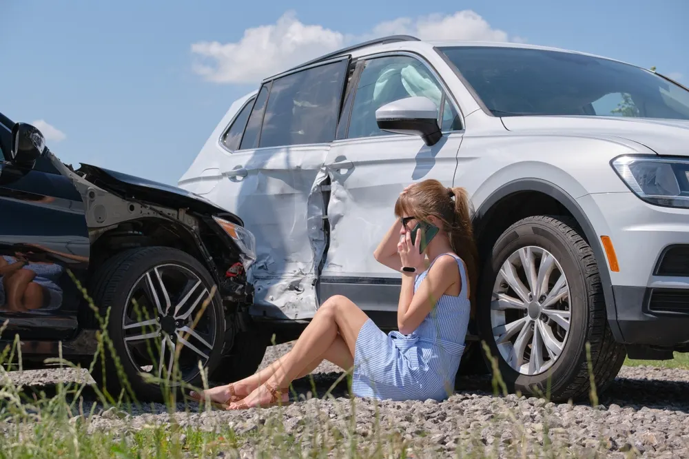 Woman sitting beside a wrecked vehicle calling for help after a crash